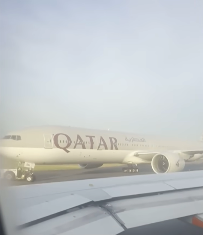 View from an airplane window of a Qatar Airways plane being towed.
