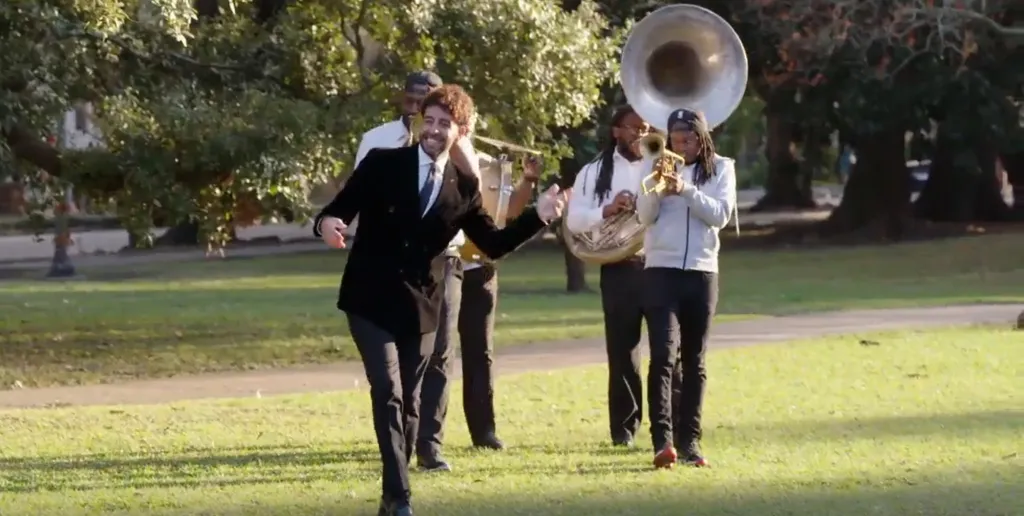 Mido dancing in a park while a brass band plays behind him.
