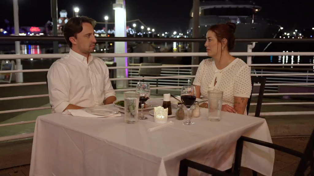 Paula and Thomas from 90 Day Fiance sitting at an outdoor restaurant table at night.