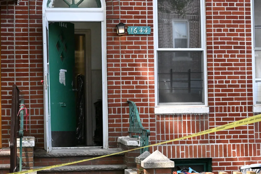 A brick house with an open green door, an outdoor light, and house number 1644, with yellow police tape across the porch.
