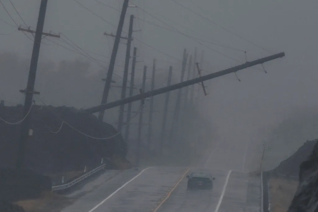 A car drives on a wet, foggy road past a downed power pole.