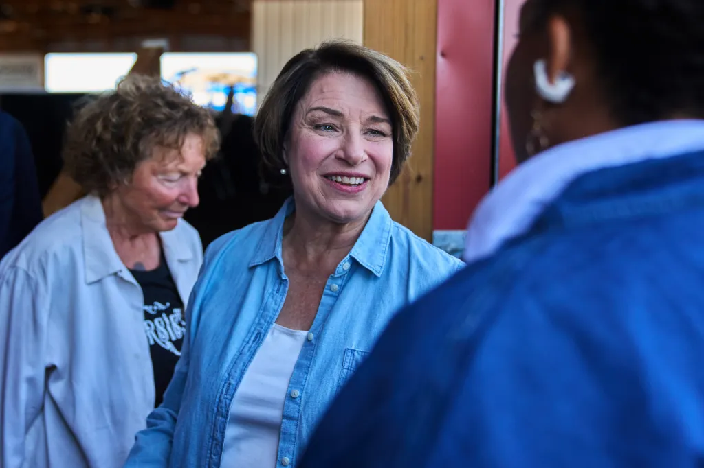 Amy Klobuchar smiling while talking to someone, with another person in the background.
