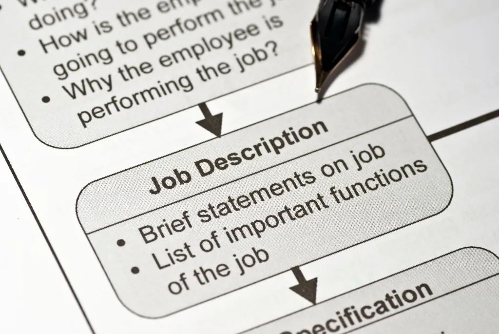 A fountain pen pointing to a job description document with bullet points about statements and functions.