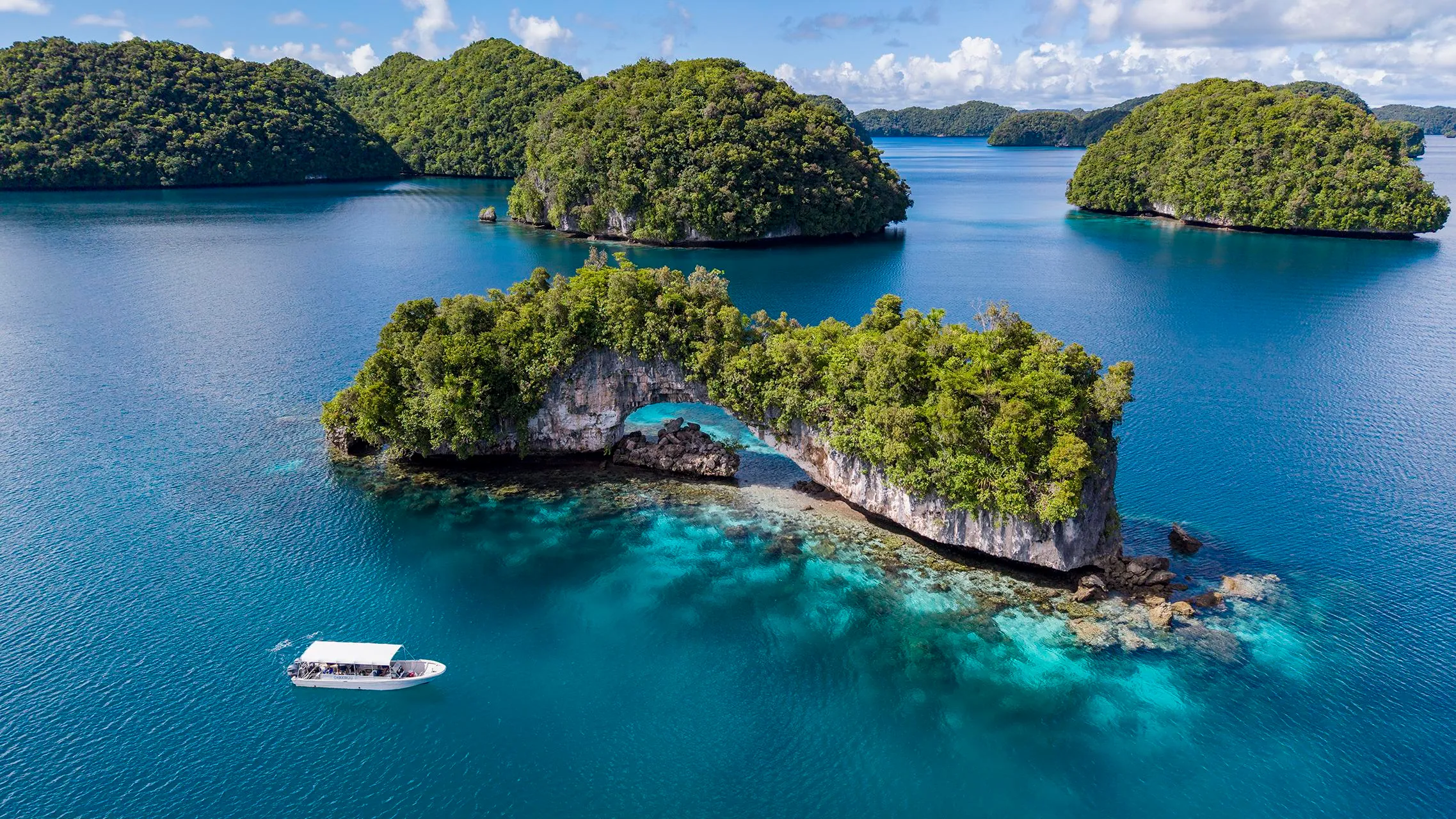 an aerial view of bright blue water with scattered, tree-covered islands