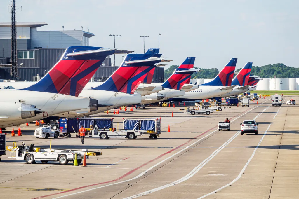 Several Delta airplanes are parked at an airport gate with ground crew and vehicles nearby.