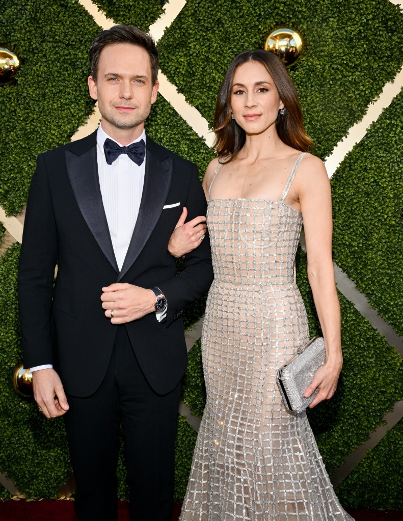 Patrick J. Adams in a tuxedo and Troian Bellisario in a grid-patterned gown pose arm-in-arm on a red carpet.