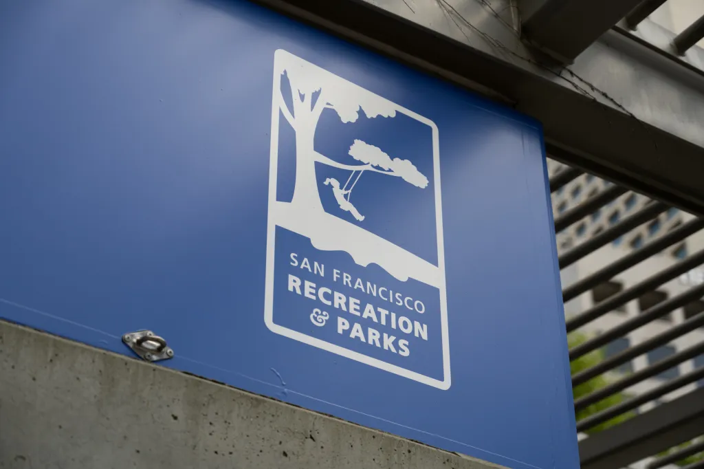 San Francisco Recreation and Parks Department sign, featuring a white illustration of a child on a tree swing against a blue background.