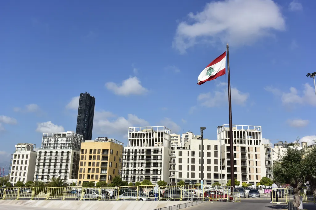 The flag of Lebanon flies over a cityscape with several buildings.
