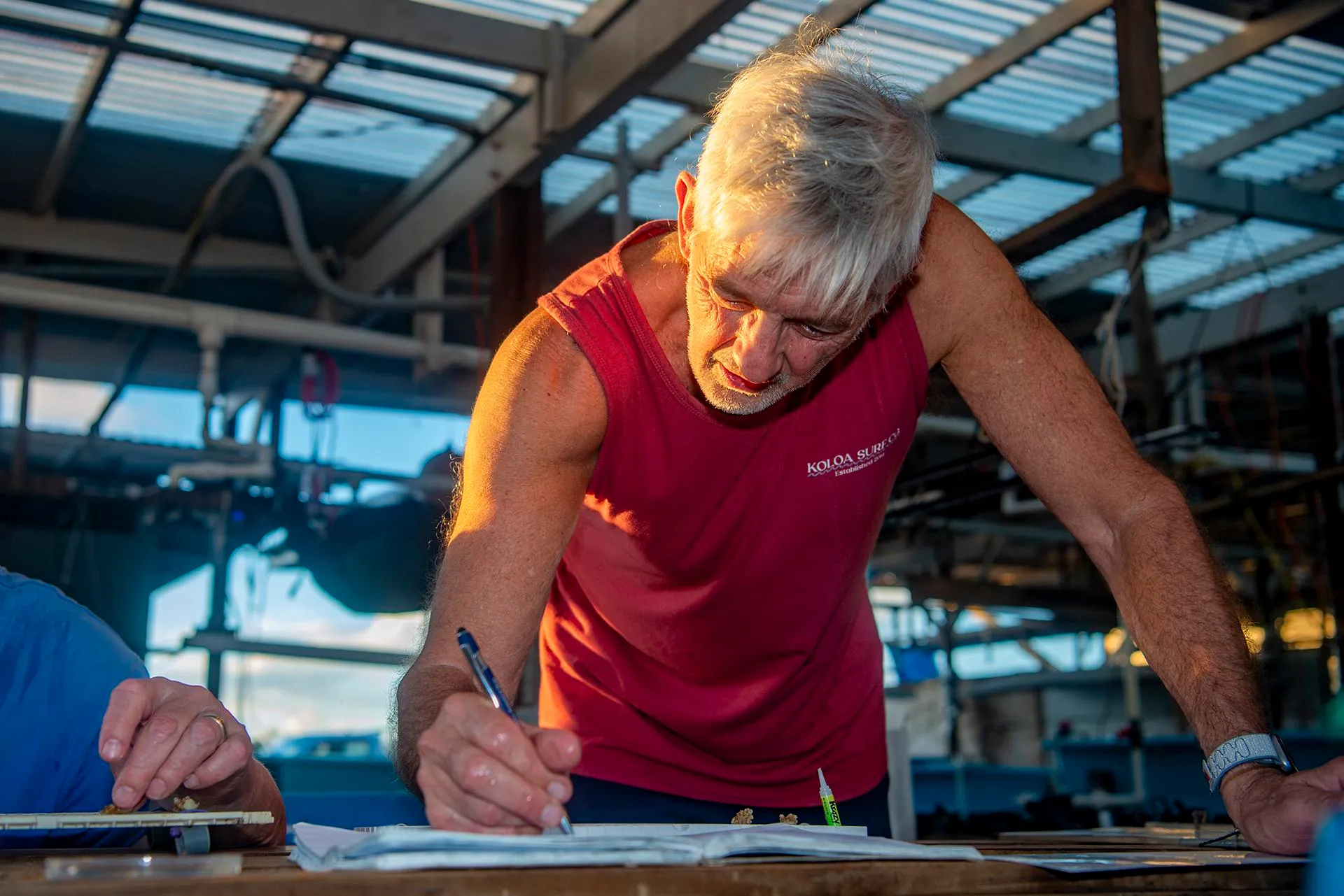 a man with white hair is intently writing notes as the sun shines brightly on the side of his face