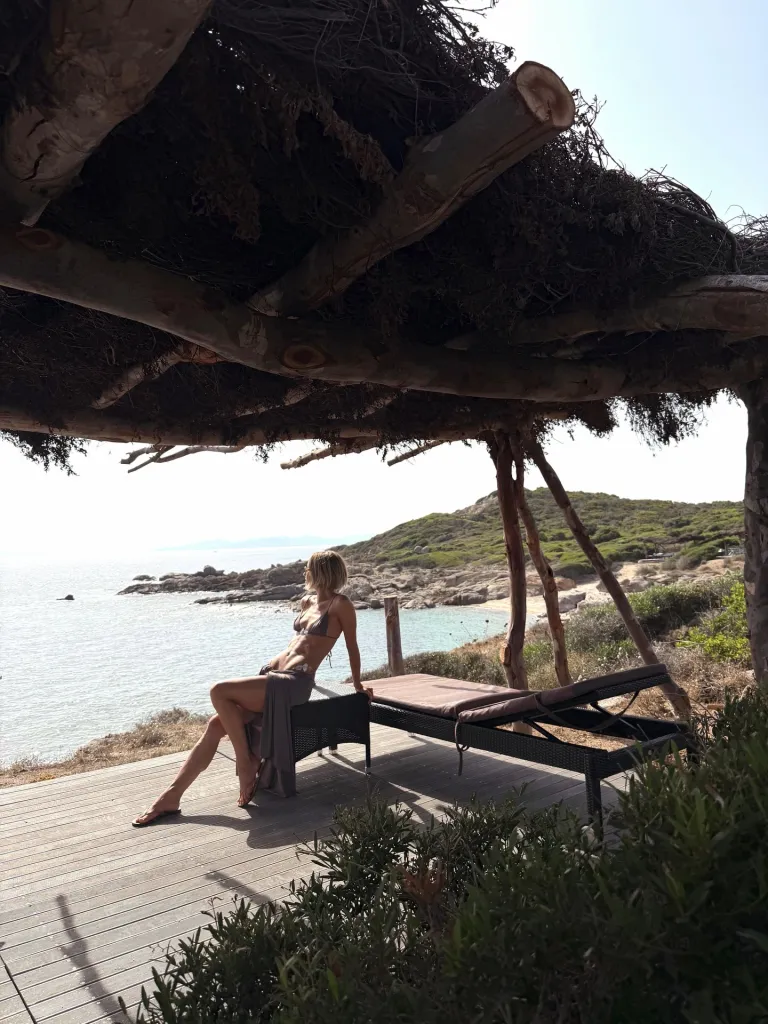 Julianne Hough in a bikini and sarong under a shaded canopy overlooking the ocean.