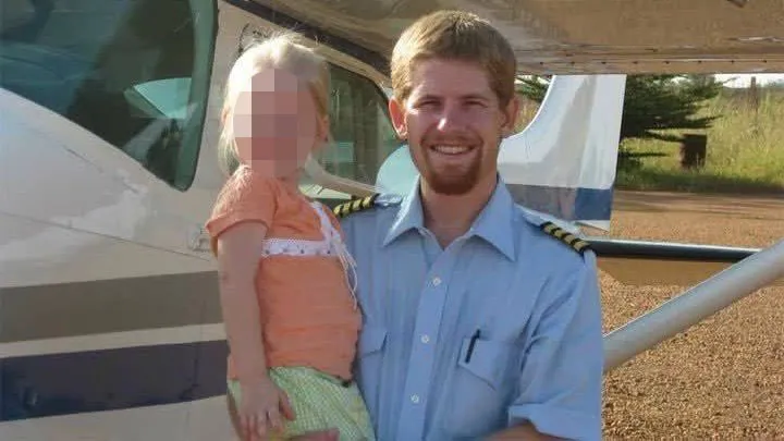 Kevin Rideout, a smiling man with a beard and a pilot's uniform, holds a young girl with a pixelated face in front of an airplane.