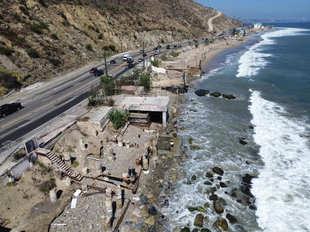 Aerial view of Malibu's coastline after the fires, showing Pacific Coast Highway, damaged structures, and the ocean.