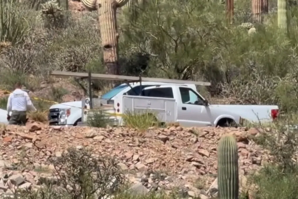 White pickup truck with a utility bed half-submerged in a ravine, with a person in a white shirt and khaki pants near it.