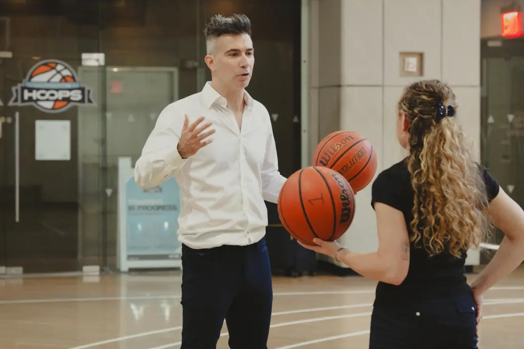 Yevgeny Dibrov speaks with a basketball in his hand to a blonde woman also holding a basketball