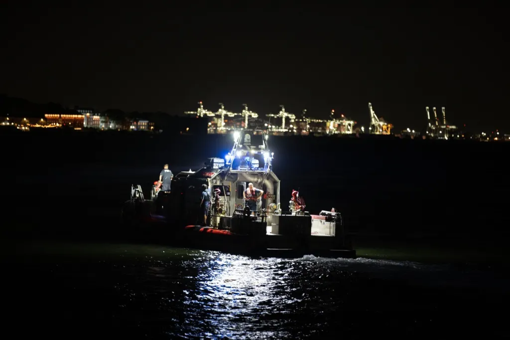 A rescue boat with crew members on board, illuminated at night with a city skyline in the background.
