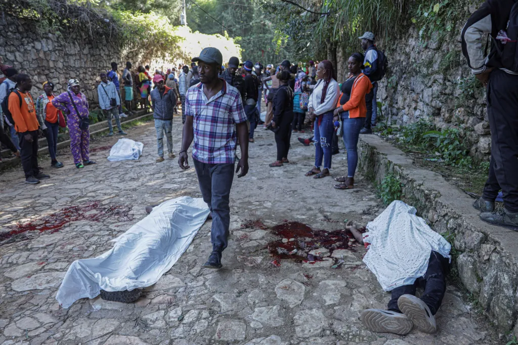 People gather around bodies covered with white sheets and blood stains on the ground after a gang attack.