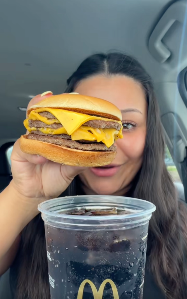 Popular food creator @theangelfoodie shows her taking a standard, golden McDonald’s triple cheeseburger and dipping it directly into a cup of ice-cold Coca-Cola.