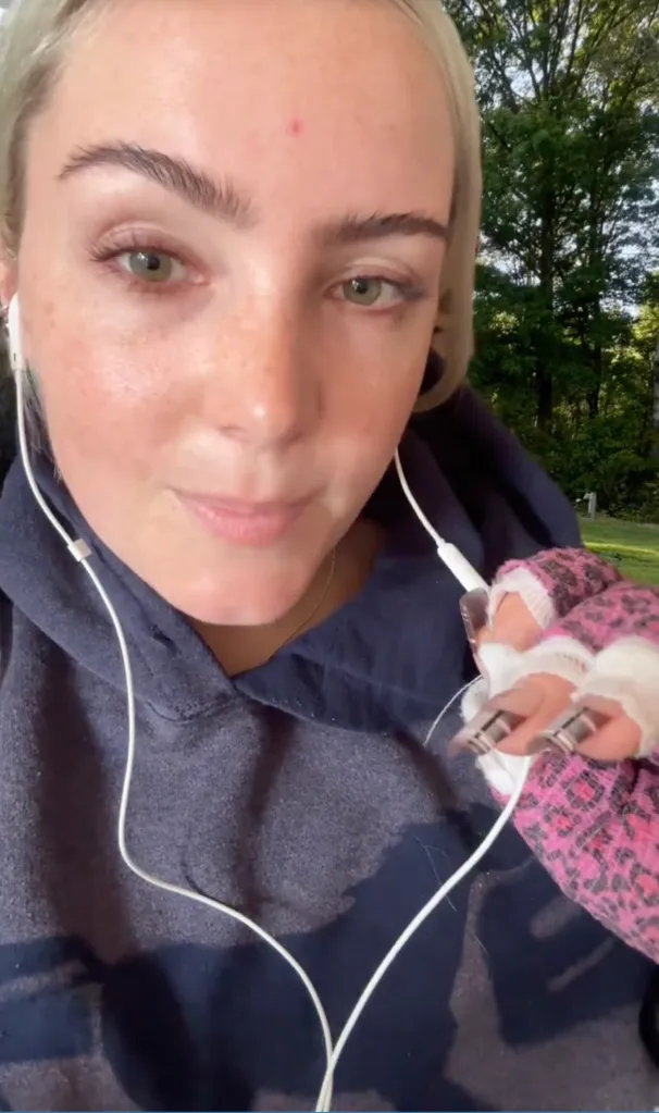 A woman wearing earphones and a blue hoodie with a pink cheetah print cast on her arm.