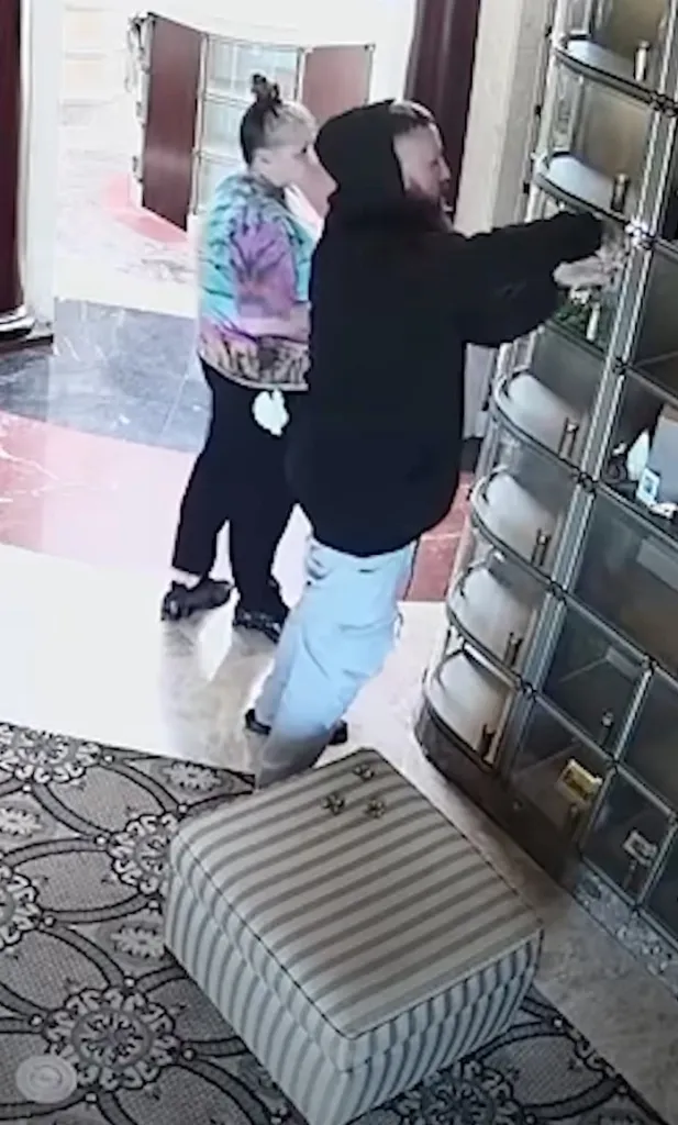 Two people standing in a room, with one person appearing to tamper with a display case.