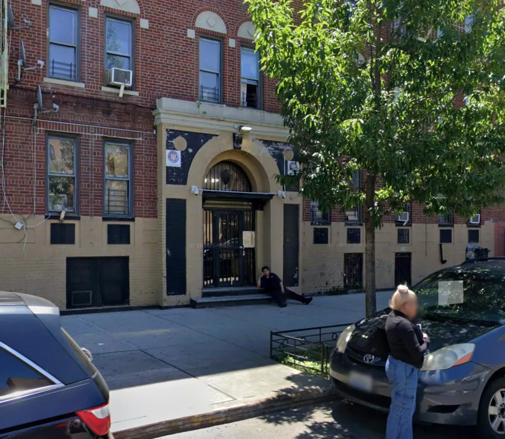 A female lying on the steps of 1236 Grand Concourse in front of a brick building.