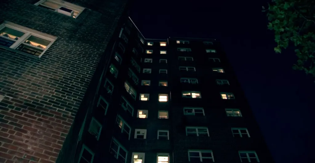 Two dark brick apartment buildings against a night sky, with some windows lit.