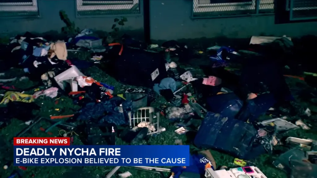 Debris, including clothing and other items, scattered across a grassy area following a deadly NYCHA fire caused by an e-bike explosion.