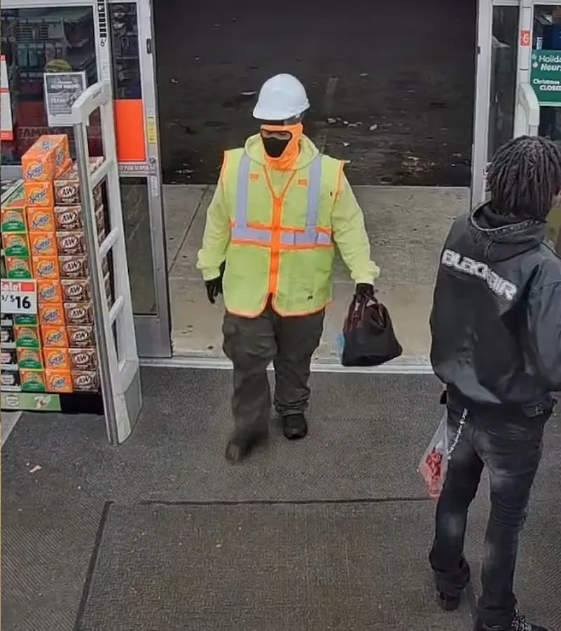 Two men, one in a construction vest and another in a black hoodie, walking into a store.