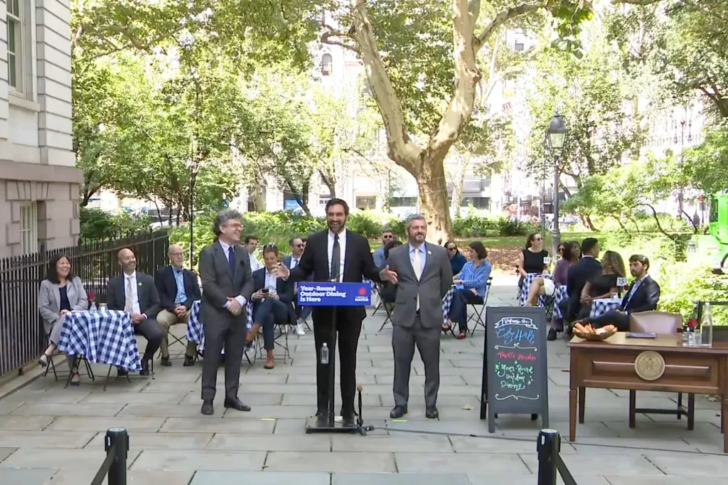 Three men speak at a podium for the 