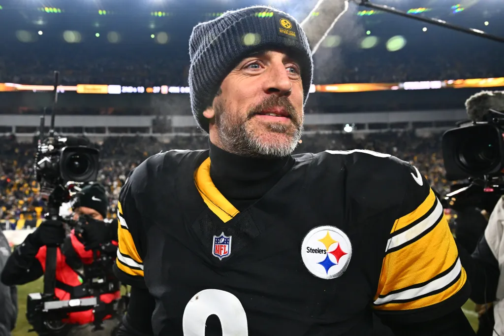 Aaron Rodgers wearing a Pittsburgh Steelers uniform and beanie, on a football field.