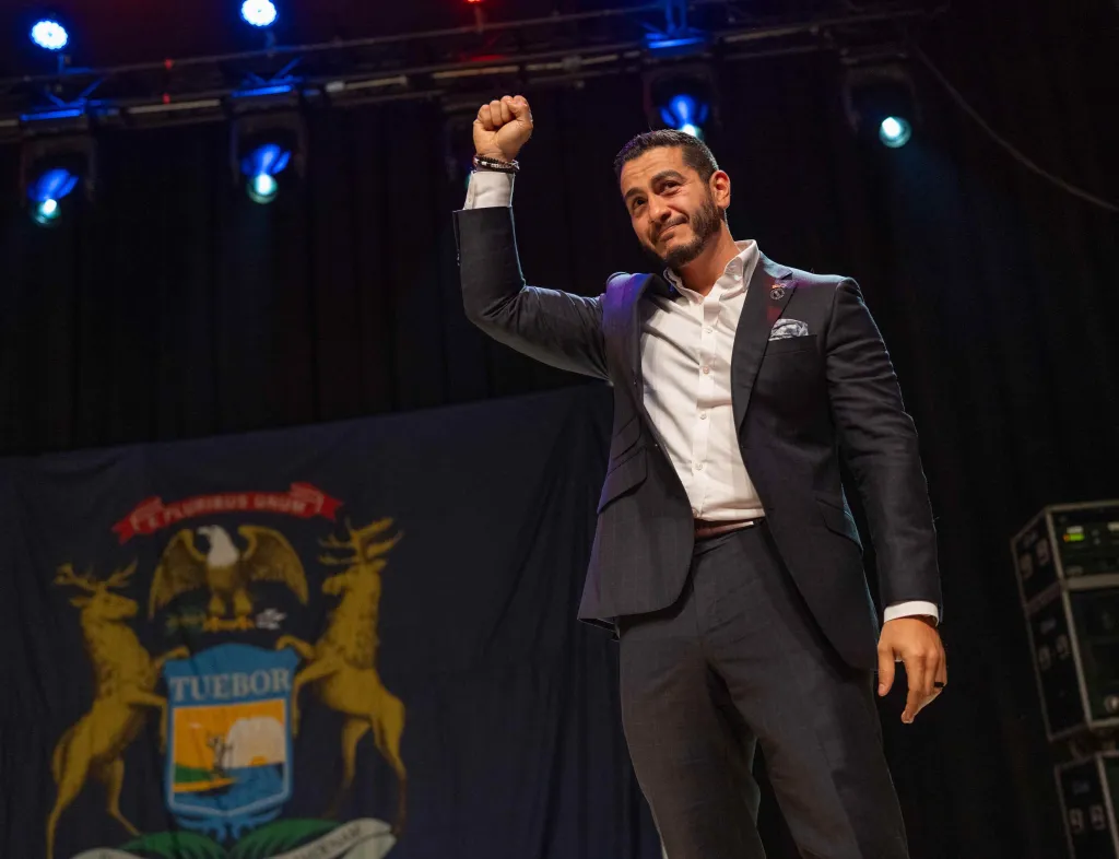 Abdul El-Sayed on stage, fist raised, addressing supporters at an election night watch party.