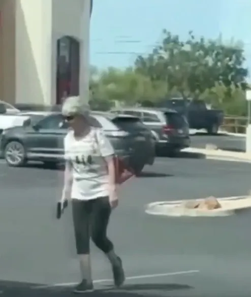 A white-haired woman with a purse holding a pistol in a parking lot.
