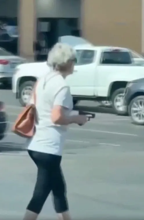 A white-haired woman with a purse holding a pistol in a parking lot.