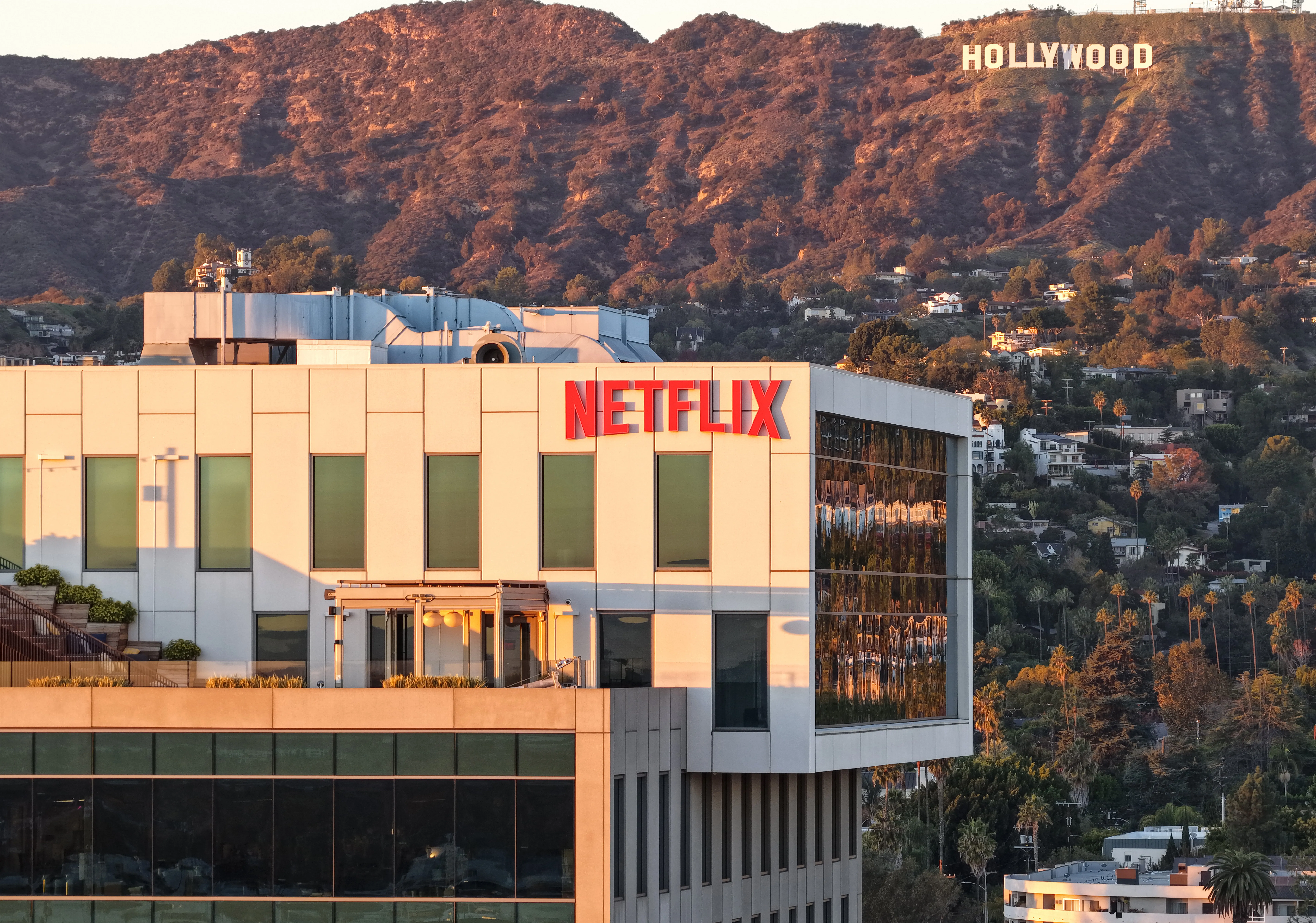 An aerial view of the Netflix logo on a building in Los Angeles, with the Hollywood sign visible in the distance.