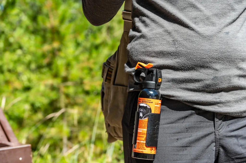 A can of UDAP Pepper Power Bear Deterrent spray being worn on a hiker's belt.