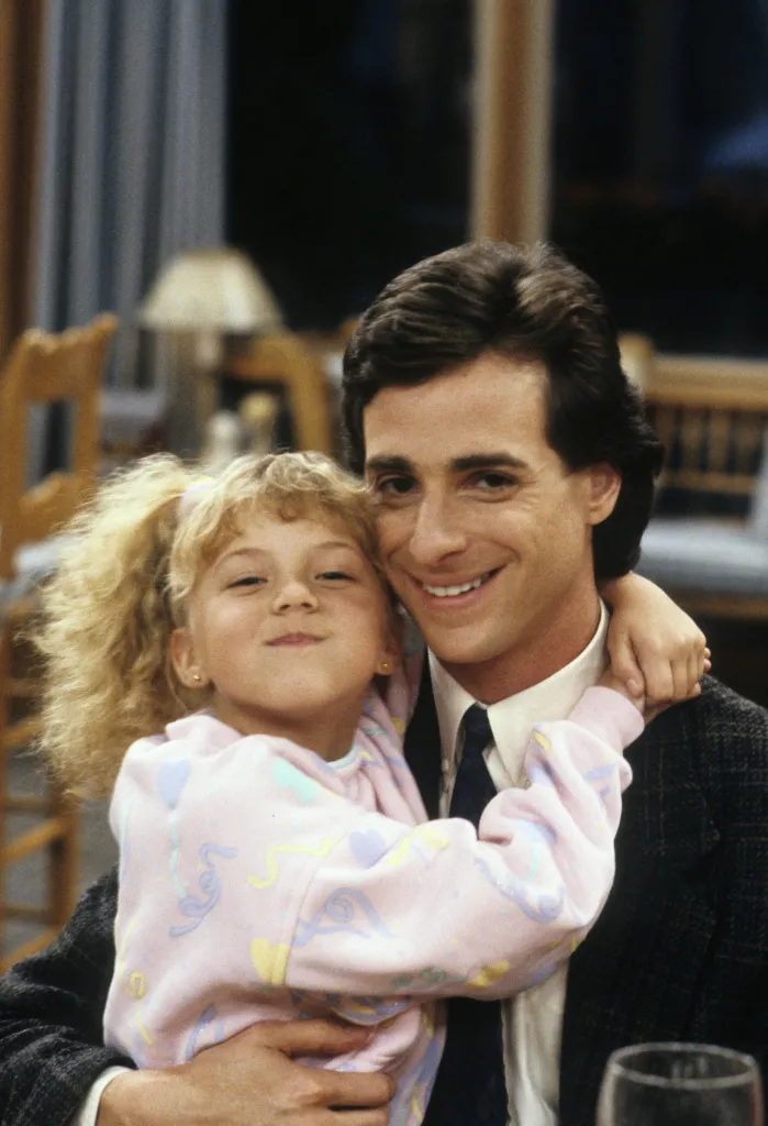 Bob Saget and Jodie Sweetin smiling, with Jodie's arms around Bob's neck.