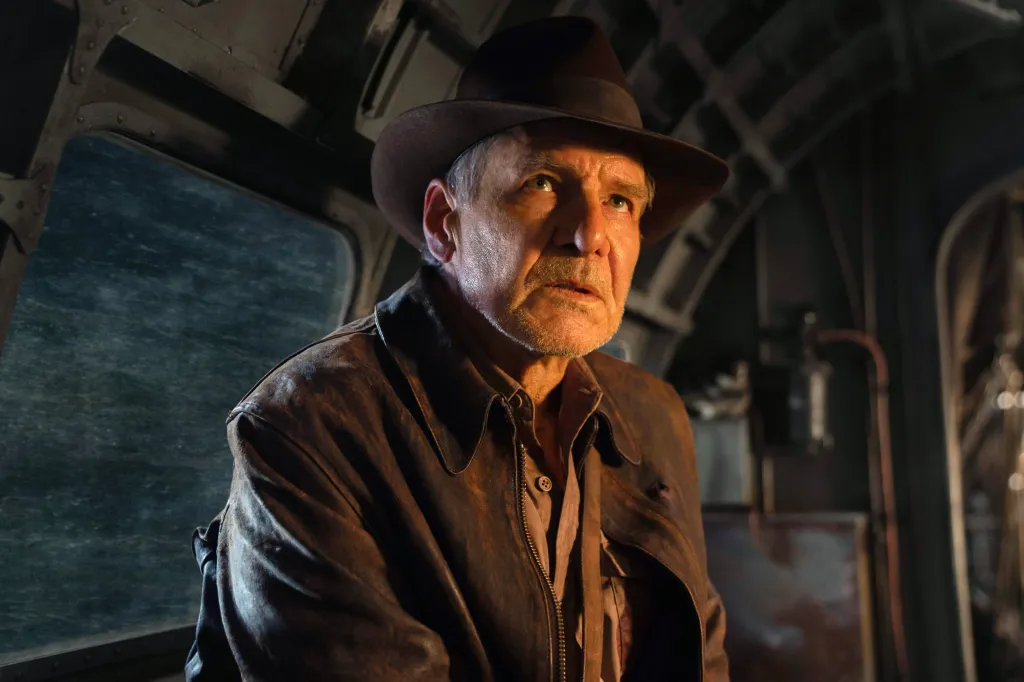 Harrison Ford as Indiana Jones in a brown leather jacket and hat, looking out of a window at a dark, stormy ocean.