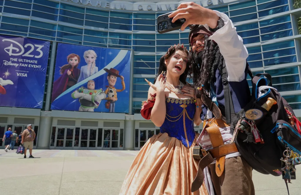 Amber Arden dressed as Snow White and Cesar Ramirez as Captain Jack Sparrow take a selfie at D23, a Disney fan event.