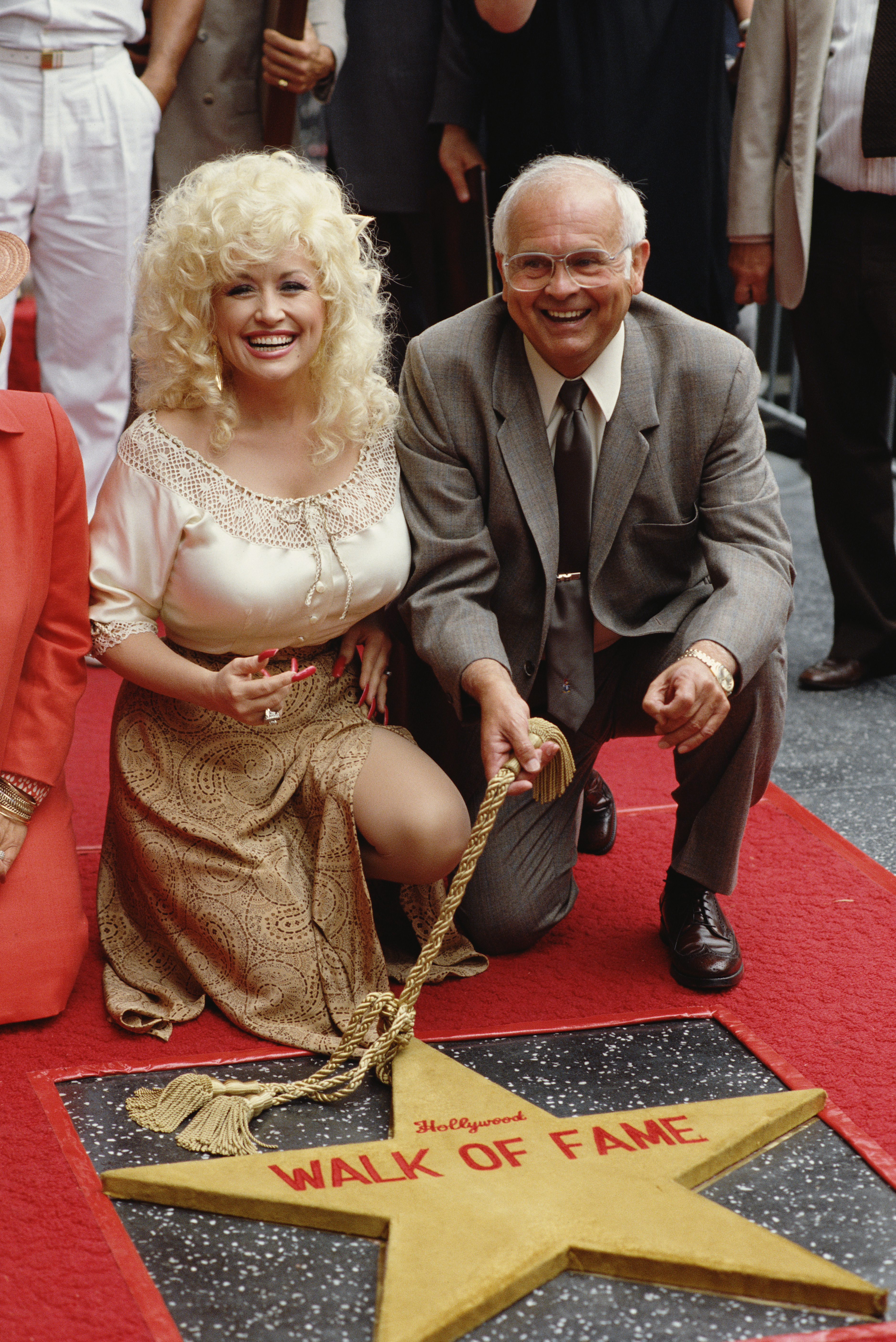 Dolly Parton and a middle-aged man kneeling next to a Hollywood Walk of Fame star.