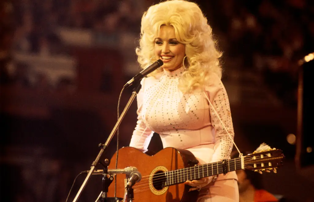 Dolly Parton performing with a guitar and microphone.