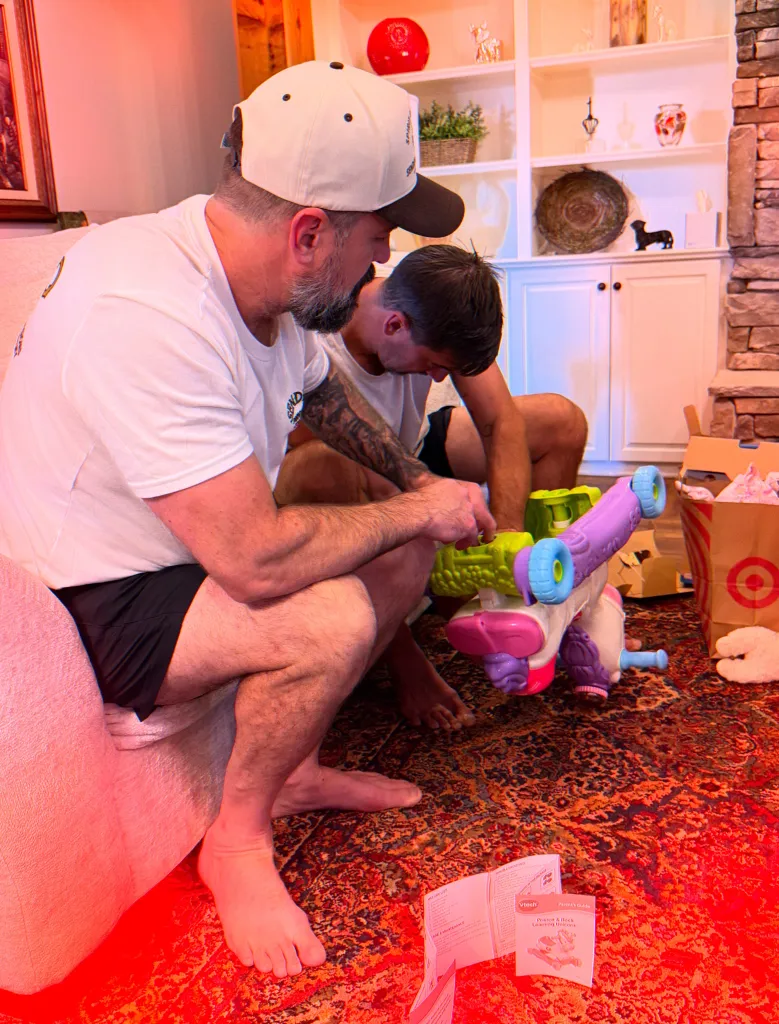 Two men on a patterned rug assembling a purple and green toy.