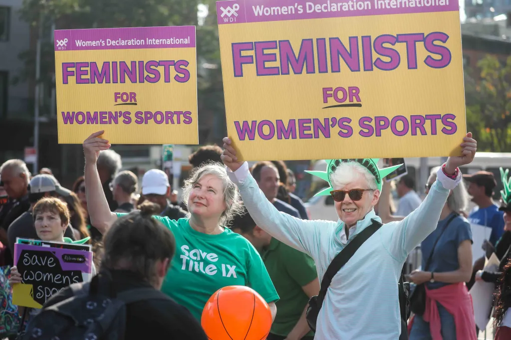 Two women at a WNBA game protest for women's sports with 