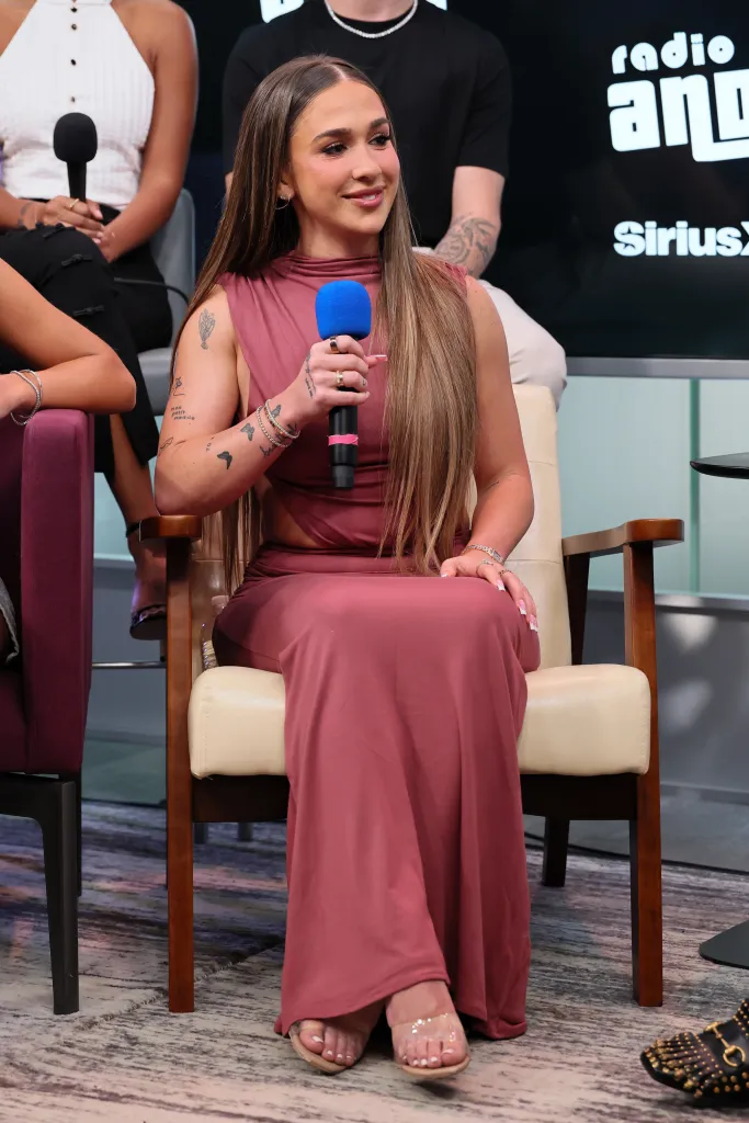 Ariana Biermann in a pink maxi dress with cut-outs holding a microphone at SiriusXM Studios.