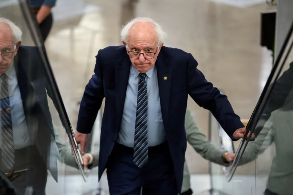 Senator Bernie Sanders ascends an escalator, looking directly at the camera with a serious expression.
