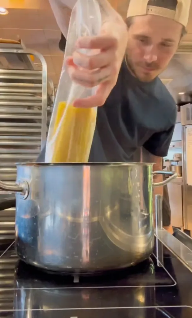 Man pouring yellow liquid from a plastic bag into a pot on a stovetop.
