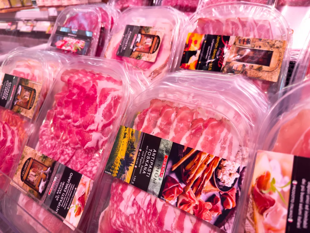 Assortment of packaged sliced meats like salami, prosciutto, and ham in a grocery store display.