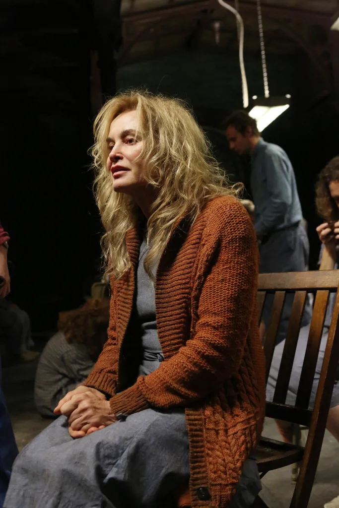 Jessica Lange in a brown sweater sitting in a chair.