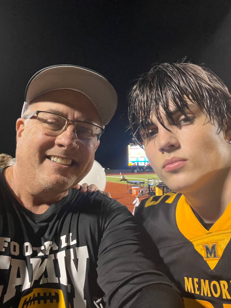 Austin Metcalf and his father smiling in a selfie at a football field at night.
