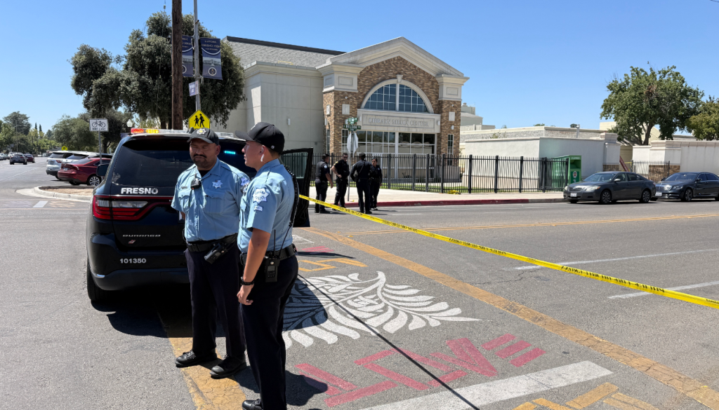 Police officers and a police vehicle behind crime scene tape at Fresno High School.