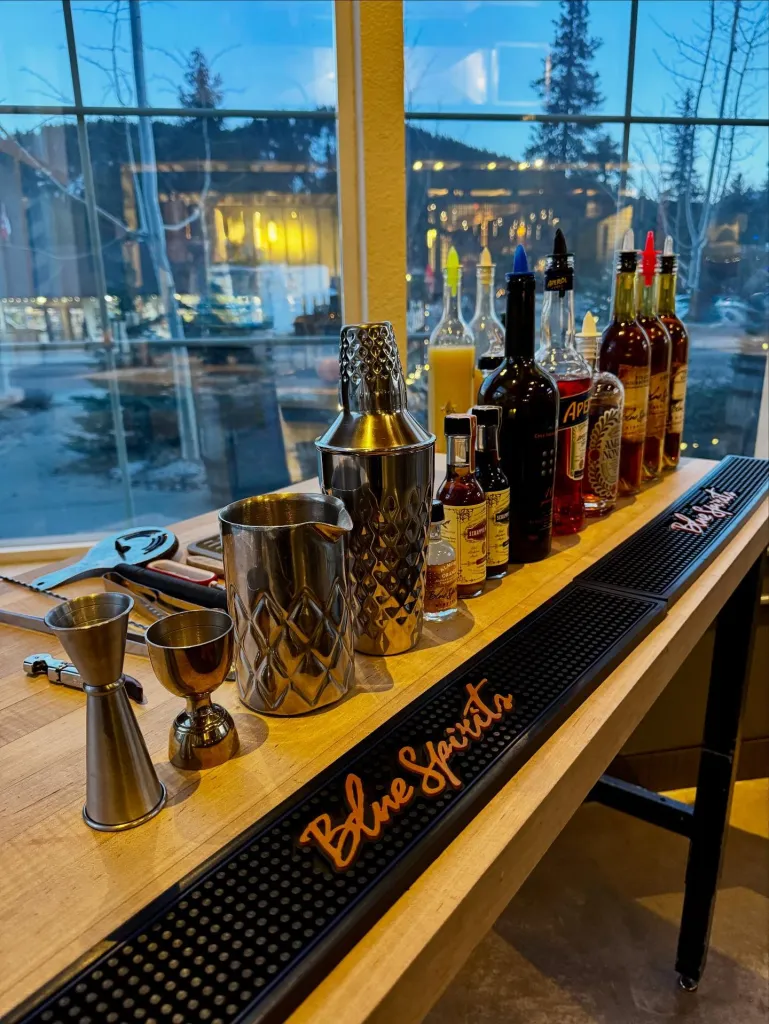 Bar counter with cocktail mixing tools, various liquor bottles, and a bar mat with 