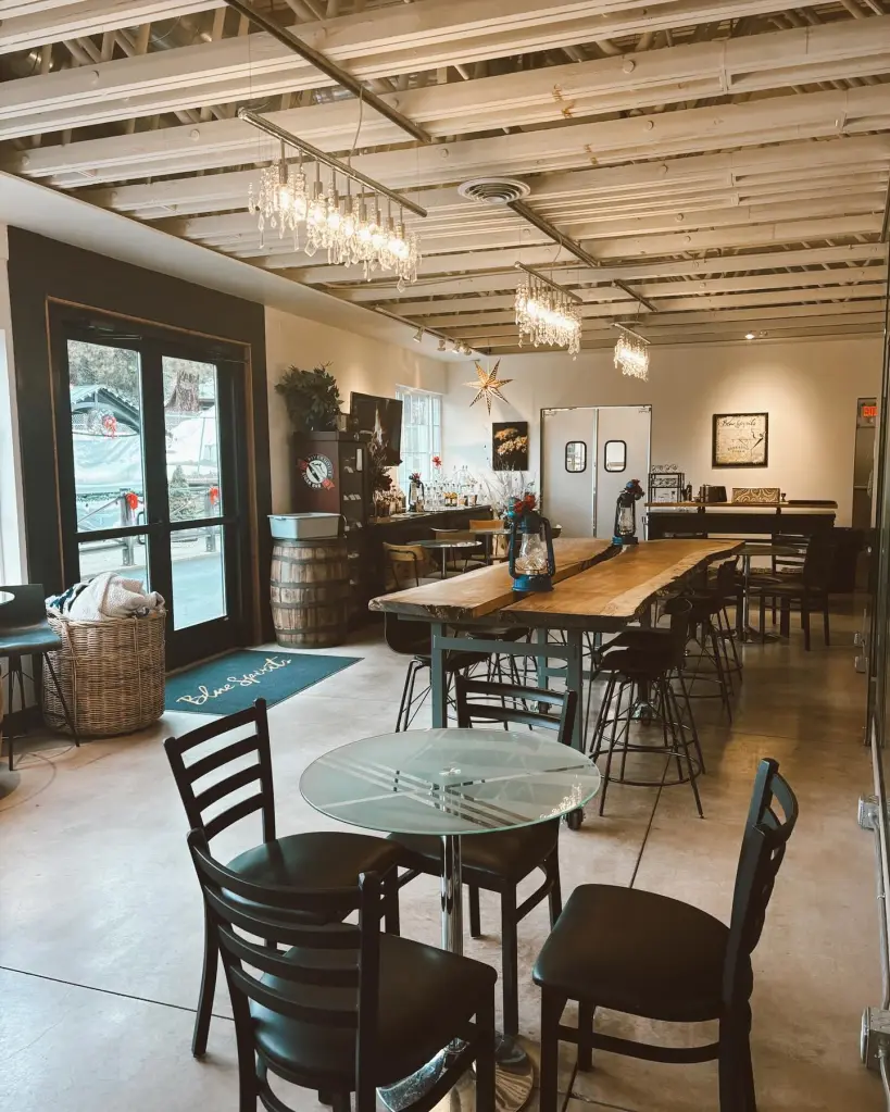 The interior of a Blue Spirits Distilling location, featuring a long communal table, smaller tables, a bar area, and exposed ceiling beams.